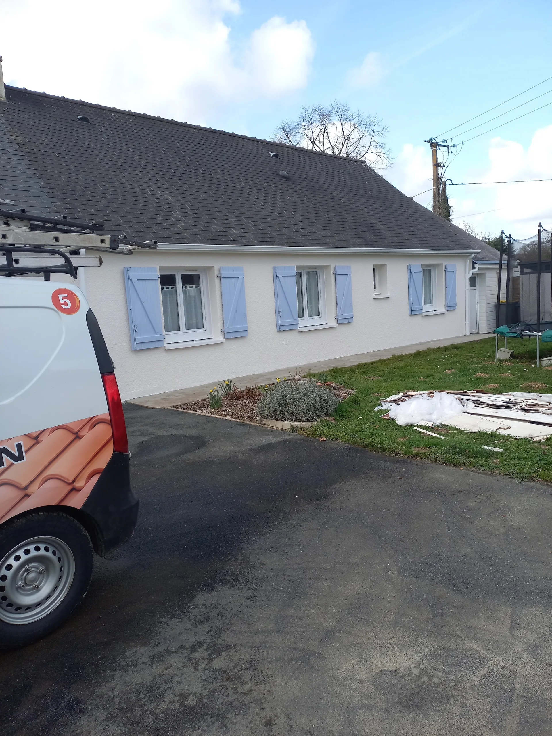 Façade blanche d’une maison, volets bleus et véhicule de chantier